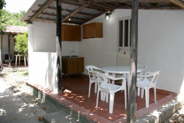 Portico con tavolo e sedie bianche in un ambiente esterno semplice.
